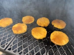 smoked pineapple slices basted in bourbon and maple syrup smoking in a smoker