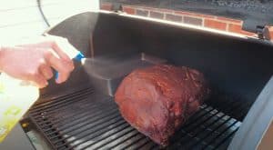spraying apple juice on pork butt while smoking on a traeger pellet grill