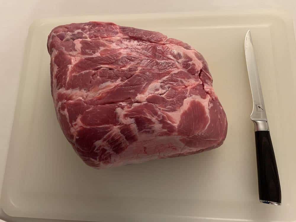 a raw pork shoulder on a cutting board