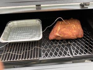 a pork butt smoking on a pit boss next to a tray of water