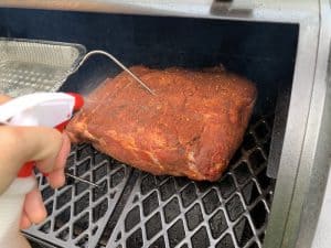 spraying cola on a pit boss smoked pork butt to keep moist