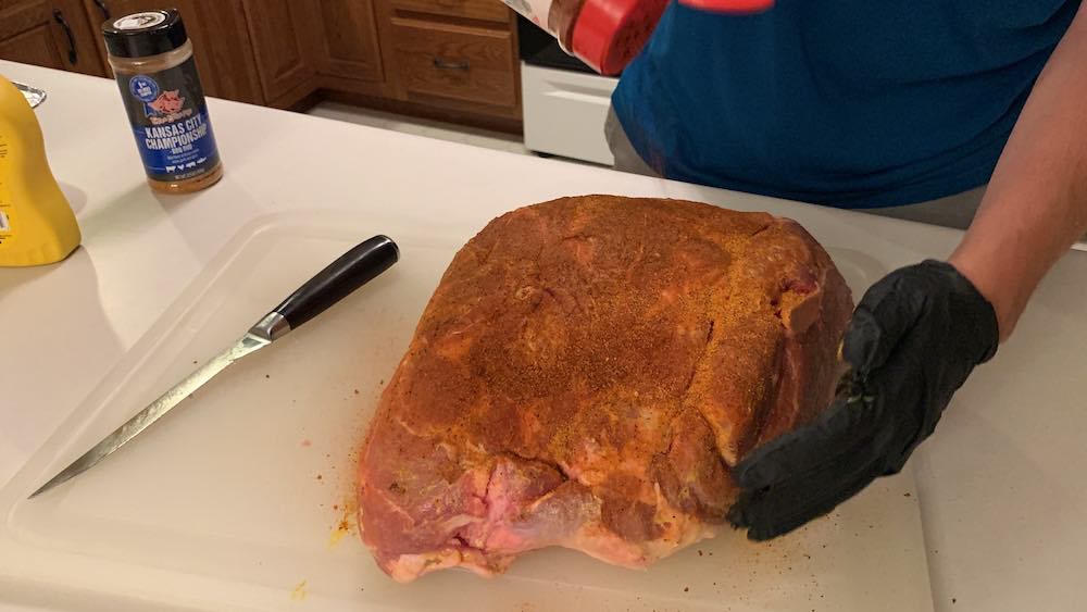 sprinkling seasoning on a pork shoulder