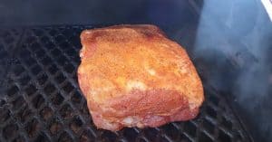a pork butt getting placed on a pit boss to start cooking