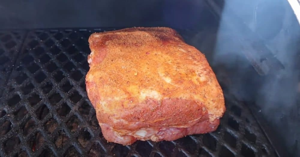 a pork butt getting placed on a camp chef to start cooking