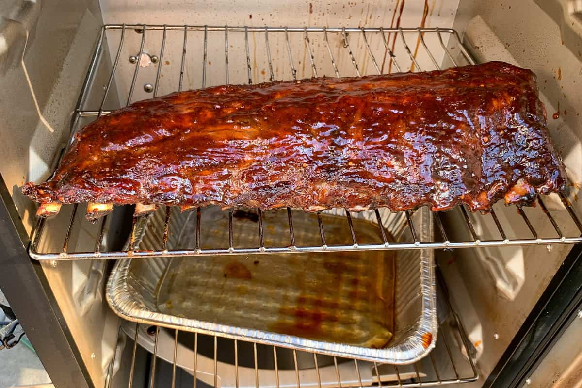 sauced ribs on the final stage of cooking on the grates of a masterbuilt electric smoker