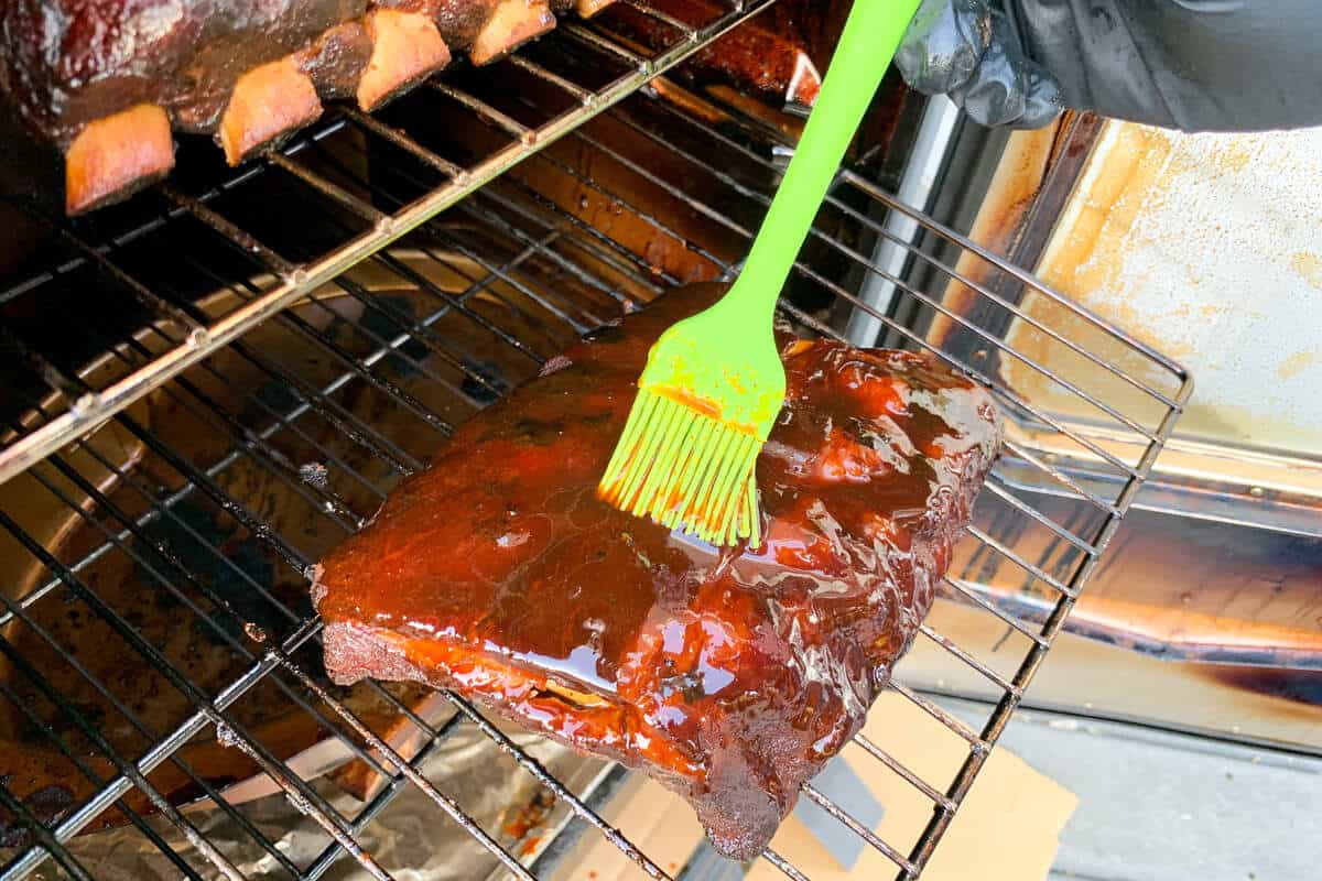 brushing BBQ sauce on ribs in an electric smoker