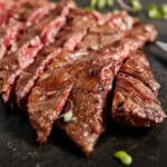 smoked flank steak sliced on a black cutting board
