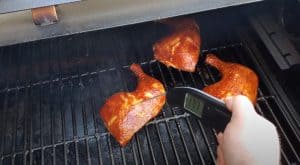 checking the temperature of chicken leg quarters on a smoker