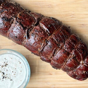 smoked beef tenderloin on a cutting board with a bowl of Dijon horseradish cream