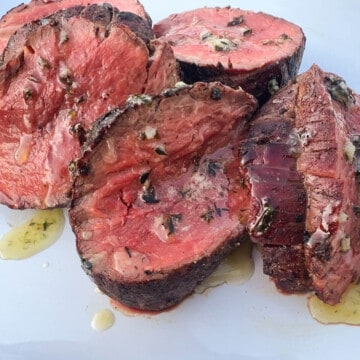 slices of Traeger smoked beef tenderloin on a white place with a melted garlic herb butter on top