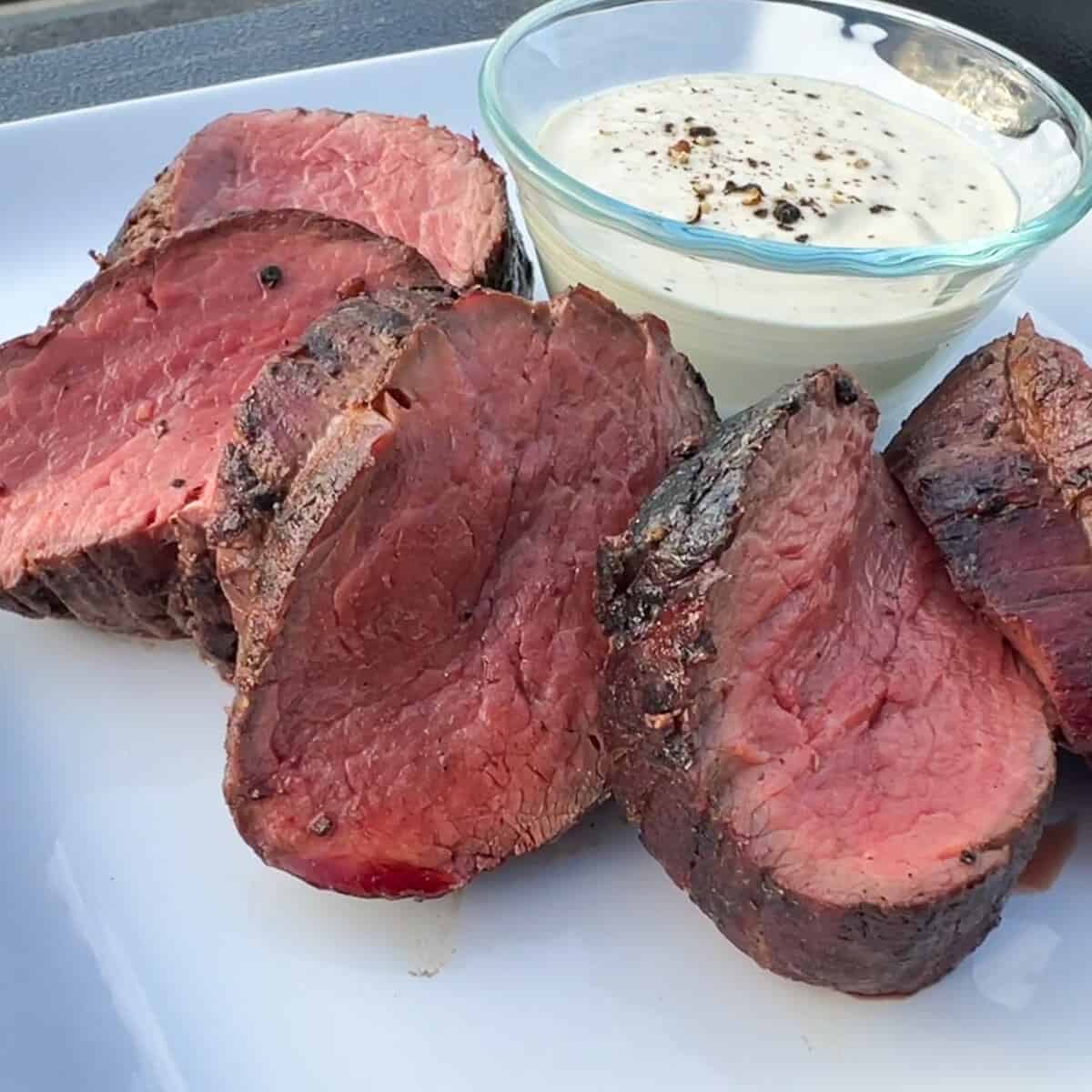 slices of smoked beef tenderloin on a white plate with a bowl of horseradish cream sauce