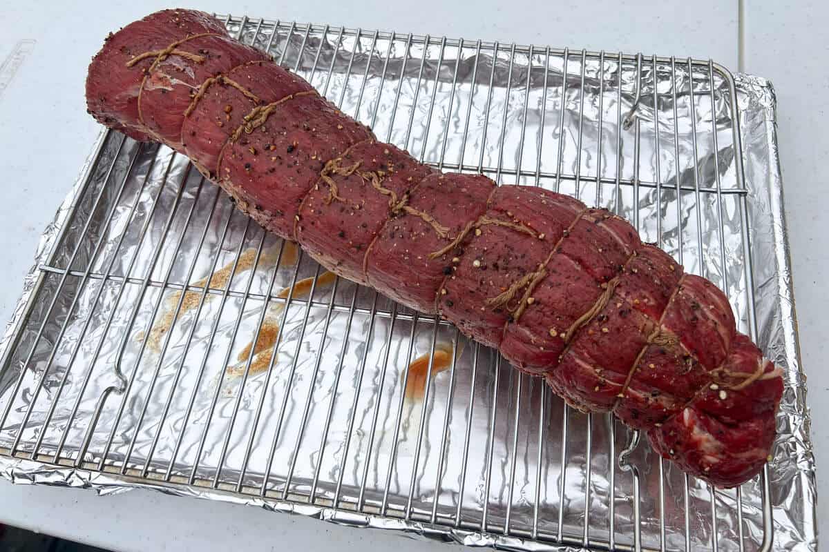 a raw beef tenderloin seasoned with Worcestershire sauce on a wire rack over a baking sheet