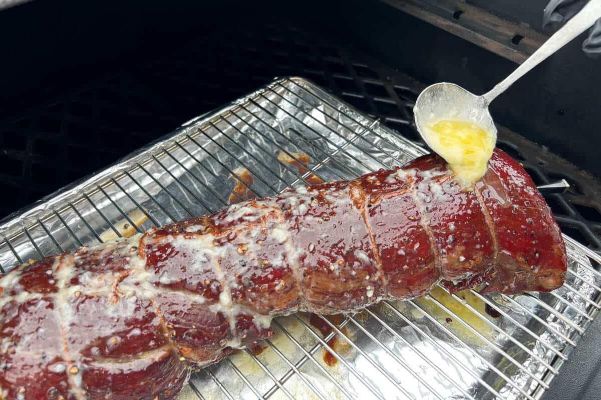 spooning garlic butter on top of a beef tenderloin on top of a wire rack