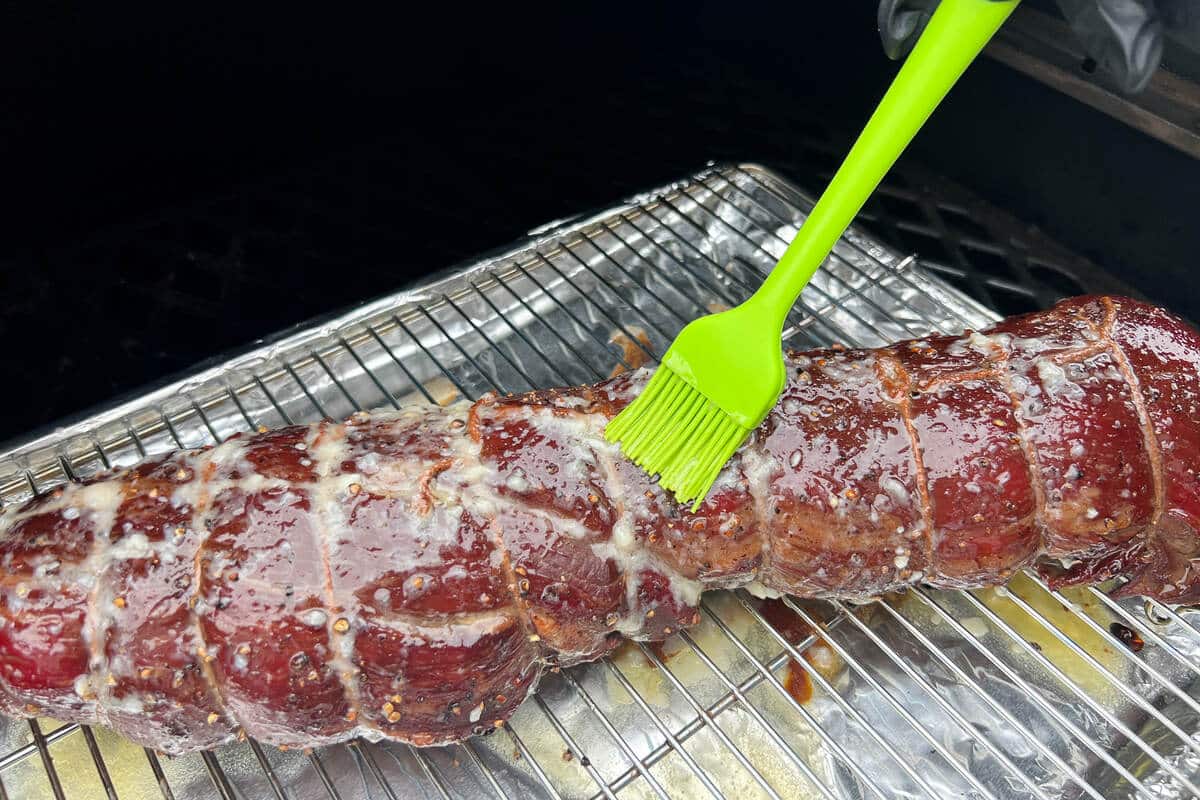 garlic butter being basted over the surface of beef tenderloin with a small silicone spatula