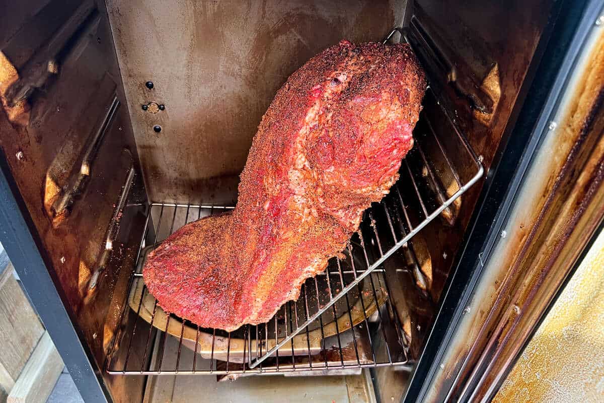 a large beef brisket placed diagonally in a masterbuilt electric smoker in order to fit