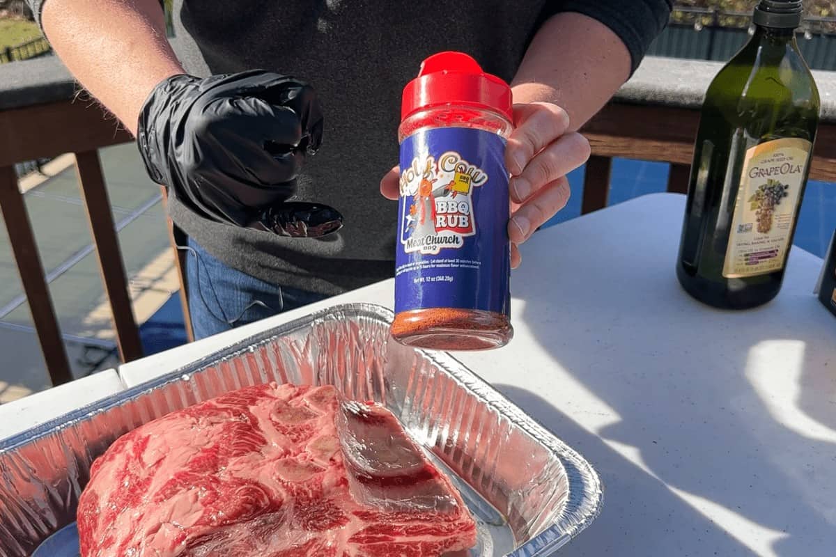 a bottle of Meat Church Holy Cow Rub held above a raw prime rib roast