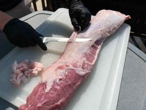 knife cutting excess fat off of a boneless pork loin