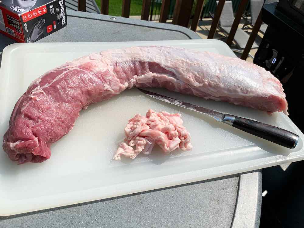 finished trimmed pork loin with a pile of trimmed fat on a white cutting board