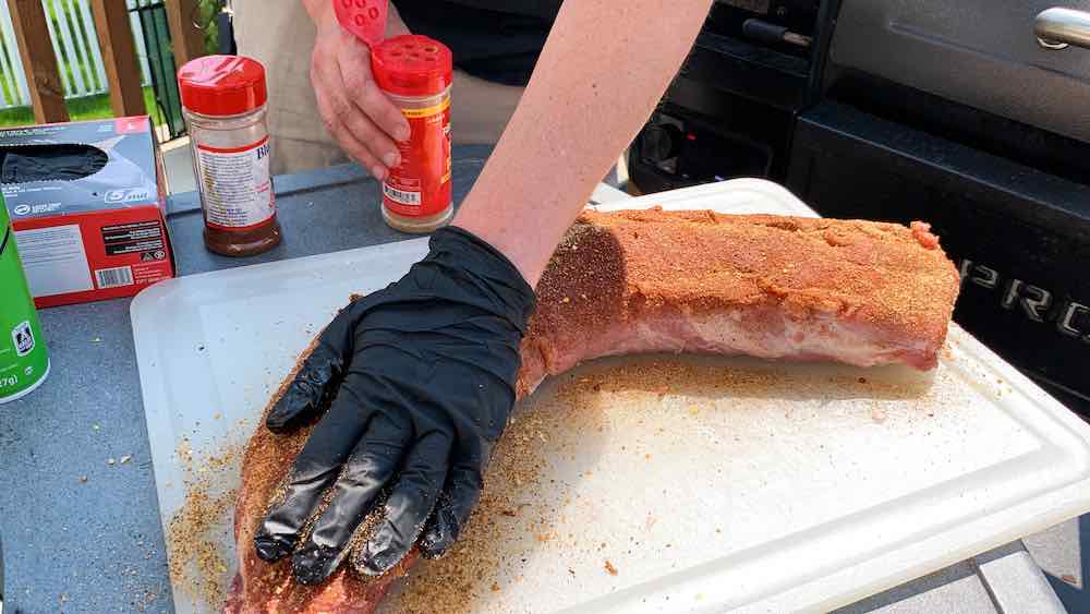 gloved hand pressing seasoning down to adhere bbq rub to pork loin