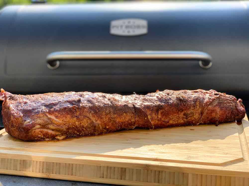 Finished smoked pork loin on a cutting board in front of a Pit Boss pellet grill