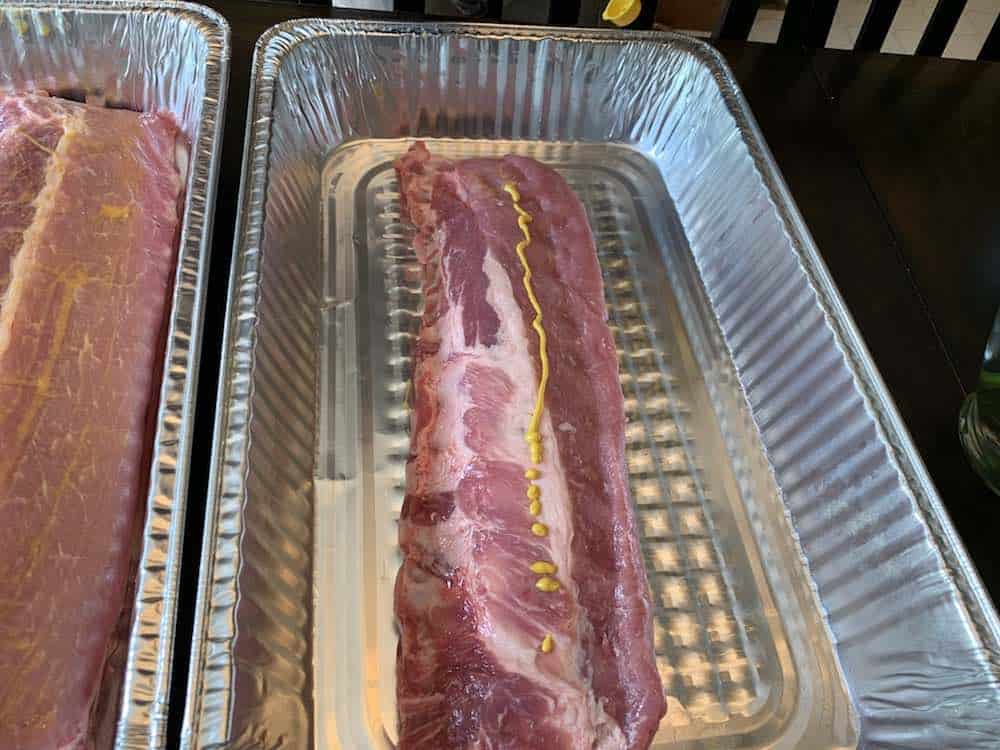 spreading mustard on raw baby back ribs for rub to stick