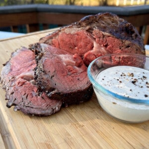 smoked prime rib sliced on a cutting board with a small glass bowl of Dijon horseradish cream sauce