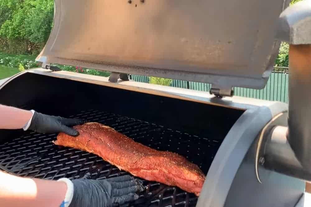 Pork loin on a pellet grill being placed with gloved hands