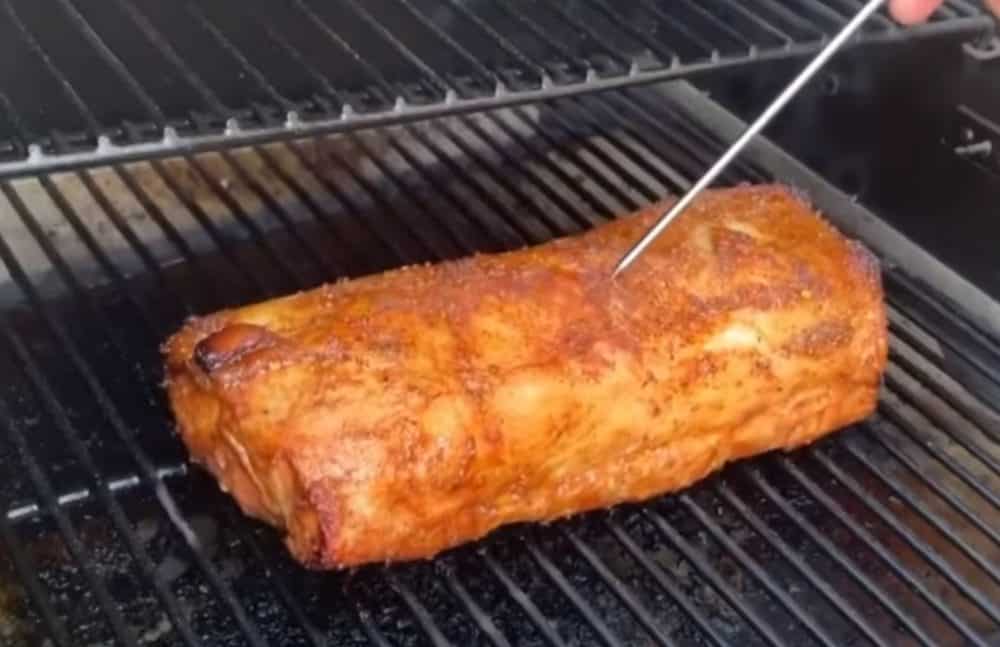 checking the temperature with a probe of a pork loin on a traeger pellet grill