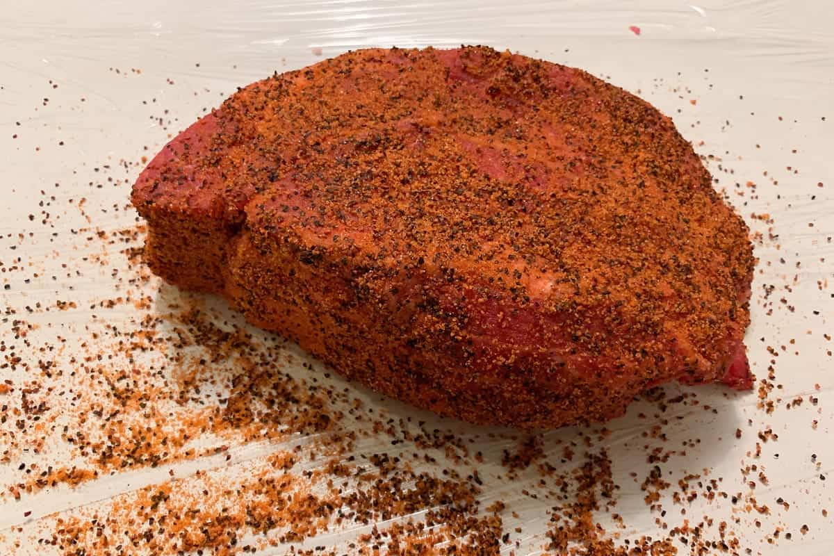 a raw chuck roast covered in BBQ rub
