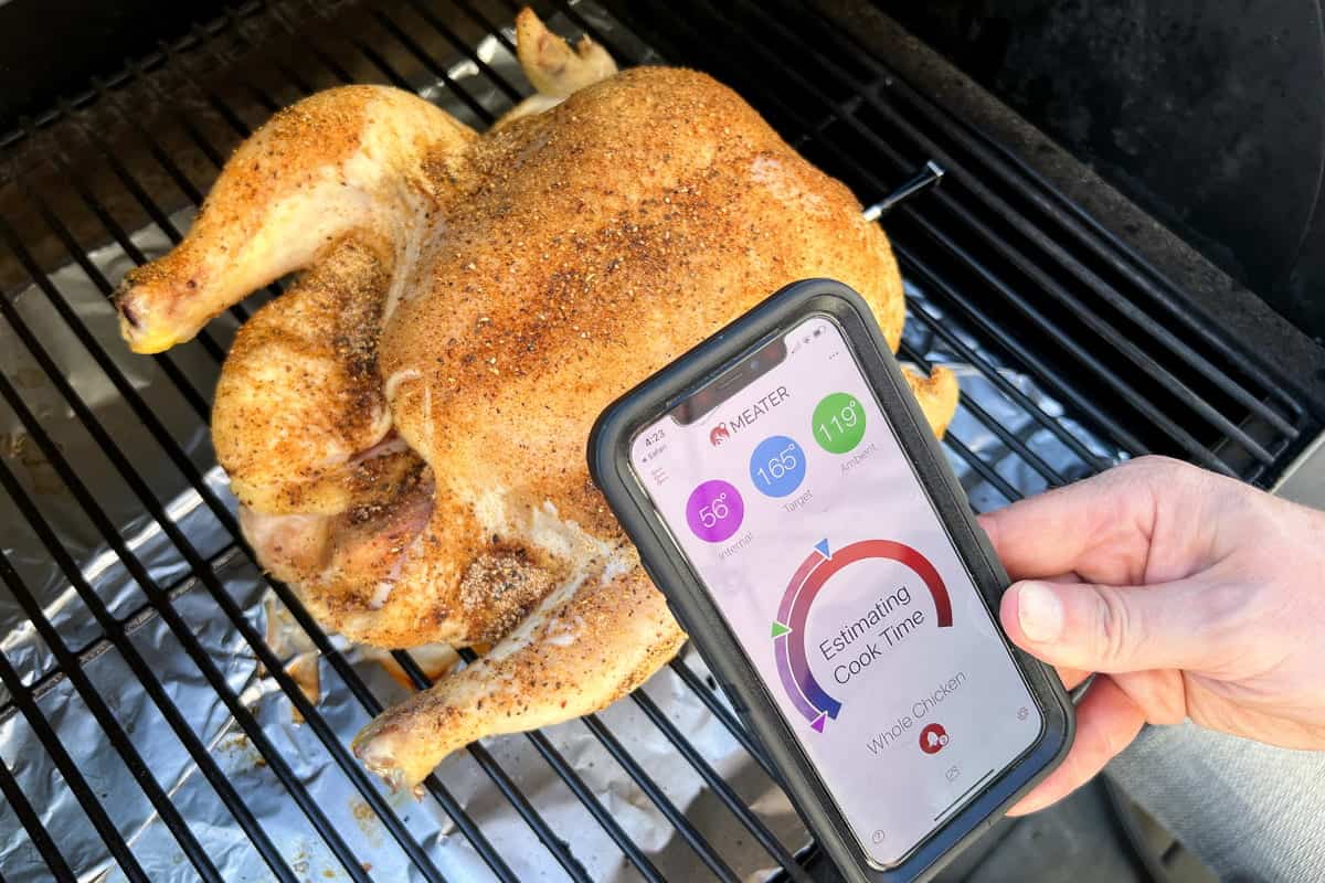 whole chicken on Traeger grates with a smart phone in front showing the MEATER thermometer app