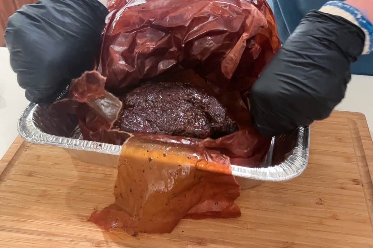 unwrapping a smoked chuck roast from butcher paper in an aluminum foil pan