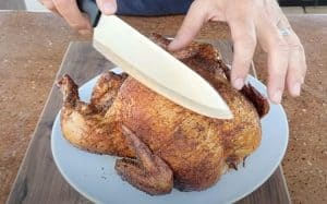 someone holding a knife getting ready to slice a smoked whole chicken