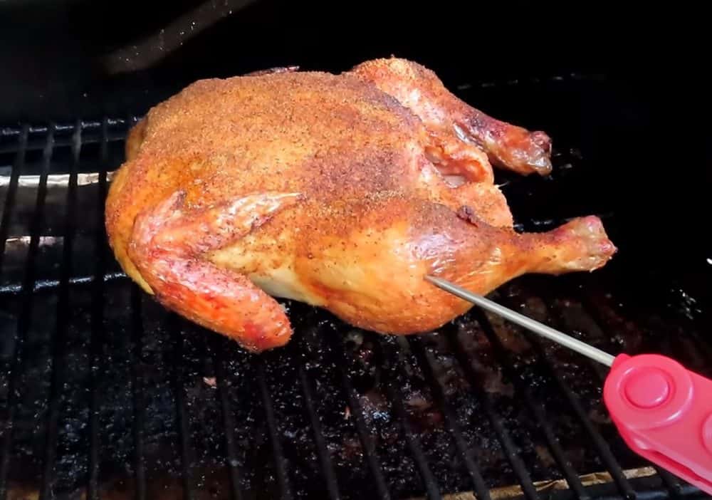 checking the temperature of a whole chicken smoking on a traeger pellet grill