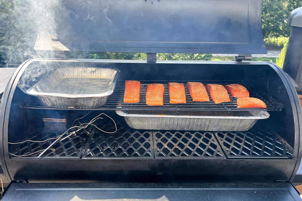 pit boss set up for smoking salmon with the salmon on the right of the top rack, a water pan on the left of the top rack, a water pan on the right of the bottom rack and a smoker box on the left of the bottom rack