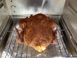 a raw chicken placed in a masterbuilt electric smoker with a temperature probe