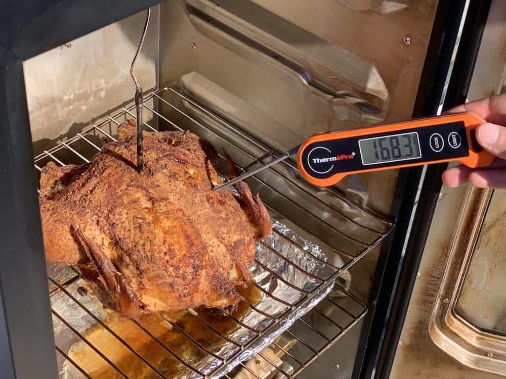 an instant read thermometer showing a whole chicken done smoking in an electric smoker