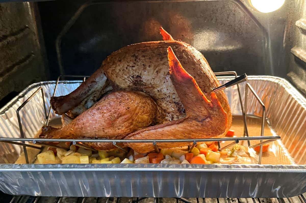 a whole turkey in a V-shaped rack set inside an aluminum foil pan with some carrots and onions