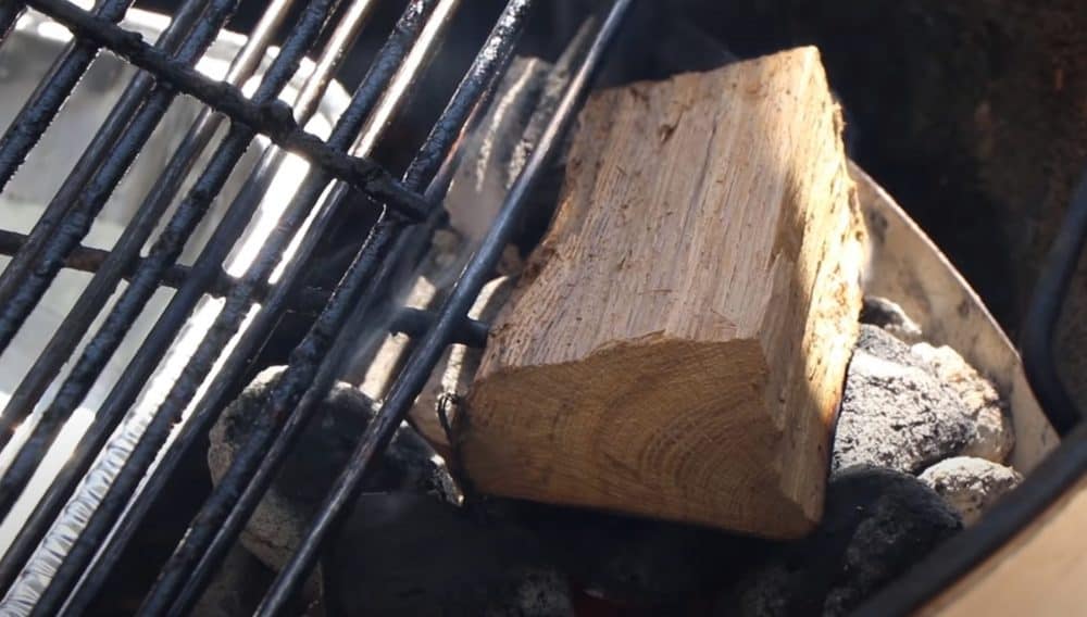 smoking wood chunk on charcoal in charcoal grill set up for indirect cooking