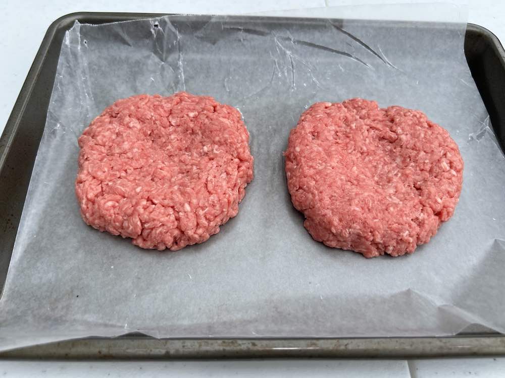 ground beef hamburger patties on a wax paper lined baking sheet