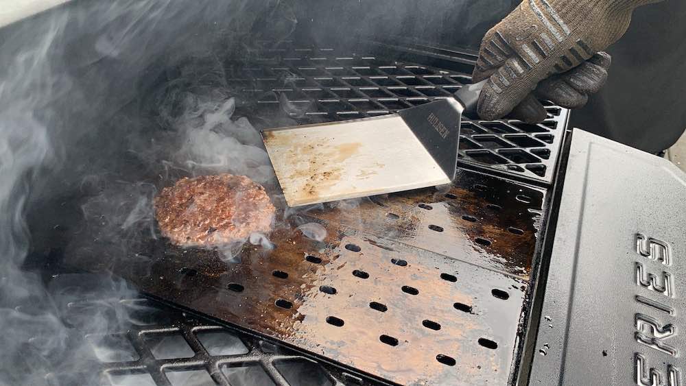 hamburger on grill grates with a heavy duty spatula