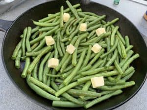 pieces of butter placed on top of a cast iron skillet full of green beans