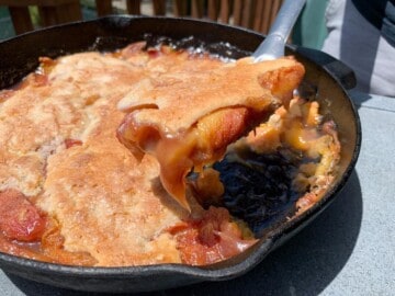 scooping out smoked peach cobbler from cast iron skillet