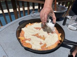 sprinkling sugar on top of a peach cobbler before smoking