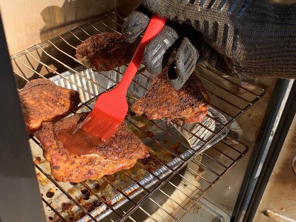 brushing bbq sauce on electric smoker smoked chicken thighs