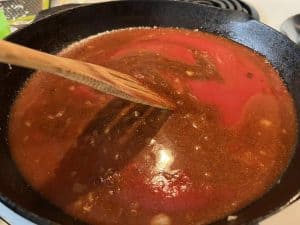 stirring in sauce for smoked chicken enchiladas in cast iron pan