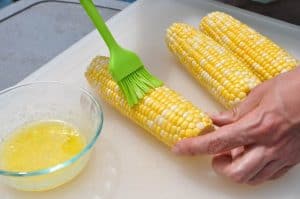 basting corn on the cob with butter and seasonings