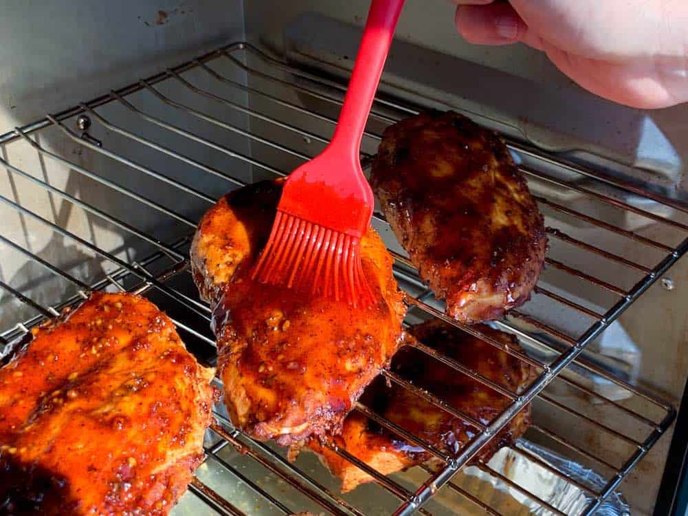 brushing barbecue sauce on chicken breasts smoking in a masterbuilt electric smoker