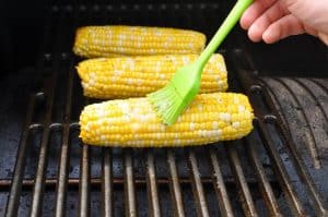 basting corn on the cob smoking on a traeger pellet grill with butter