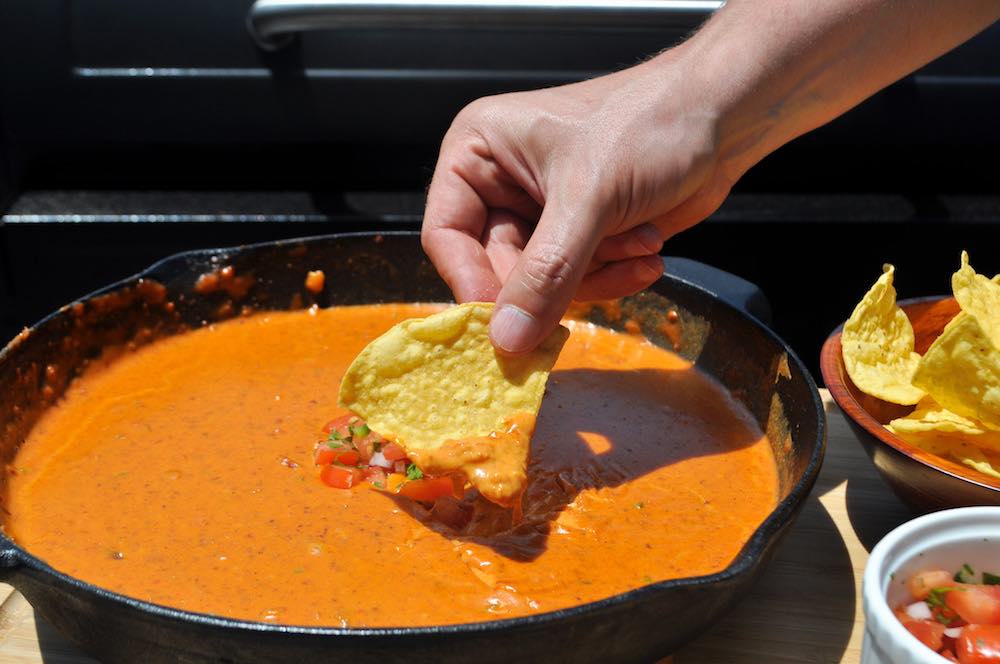 dipping a tortilla chip into a skillet of smoked queso