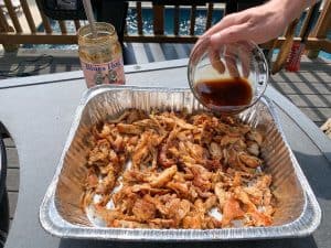 pouring sauce on smoked pulled chicken